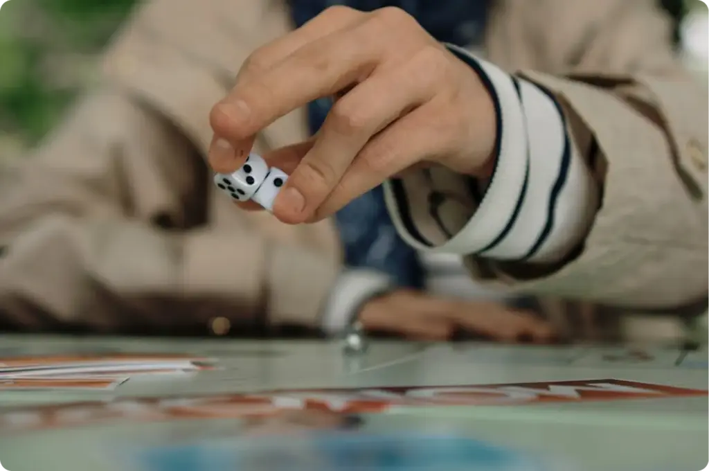 Close-up van een hand die dobbelstenen gooit bij een bordspel, waarmee een moment van spel, toeval en besluitvorming tijdens een bordspelsessie wordt vastgelegd